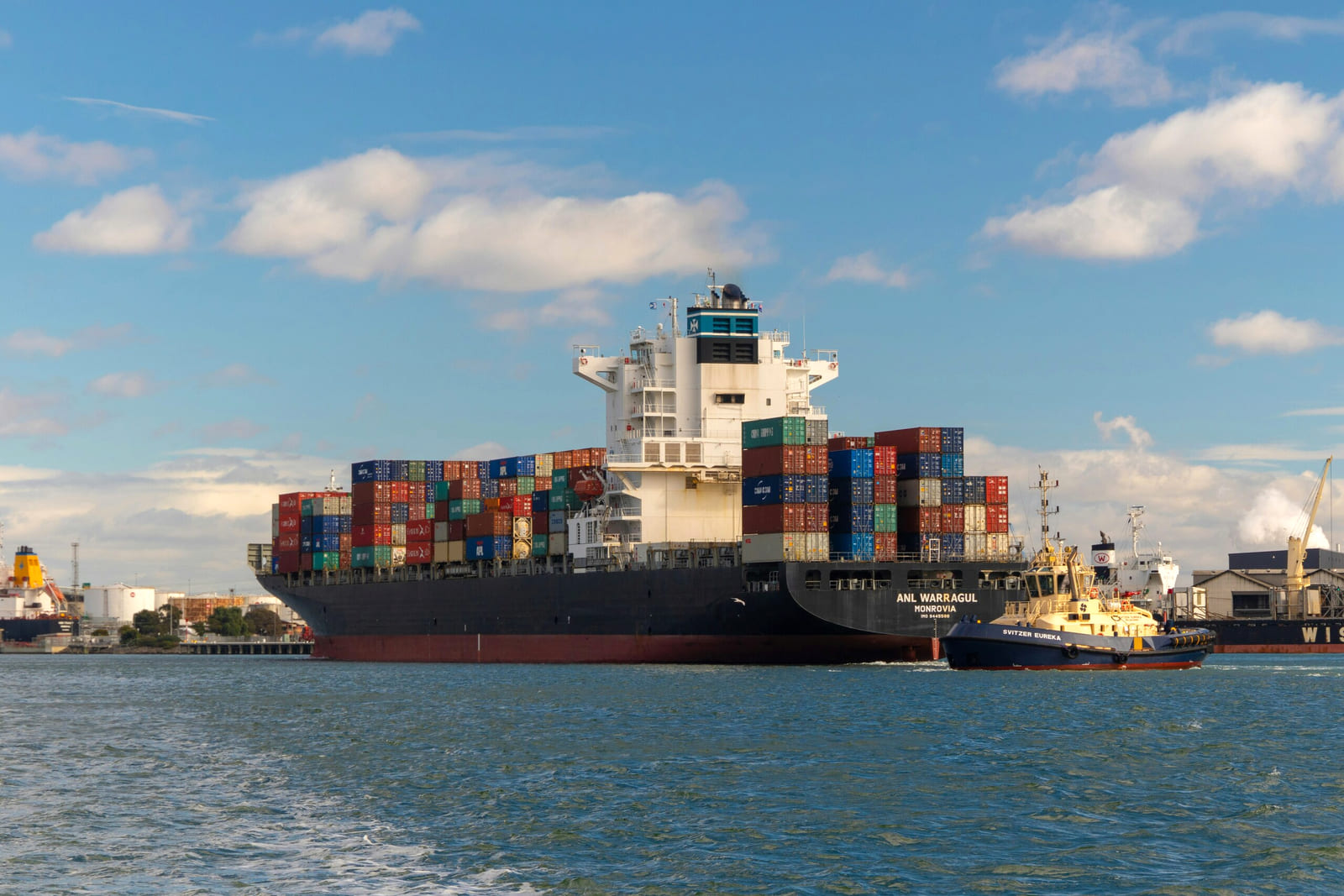 Cargo ship loaded with containers accompanied by tugboat at sea